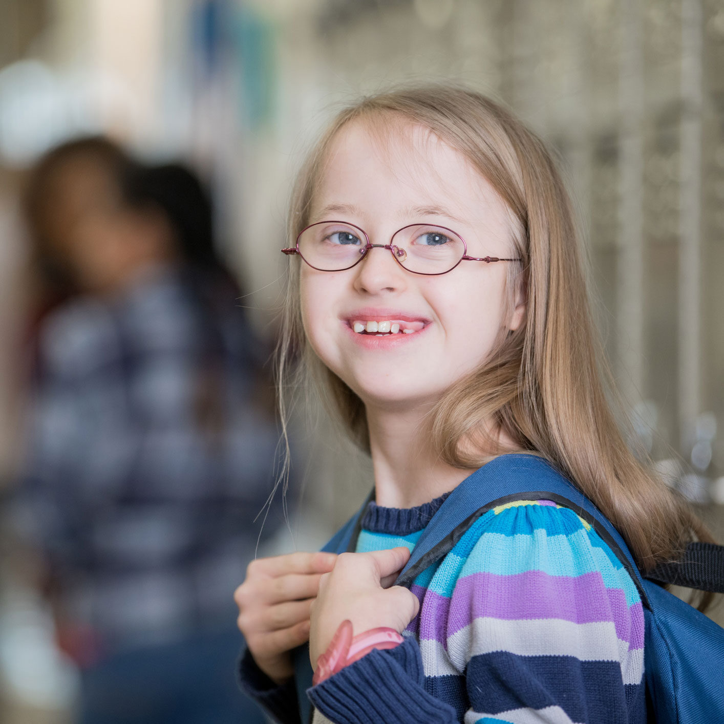 A young girl wearing glasses and a colorful backpack smiles brightly, ready for a day of adventure.