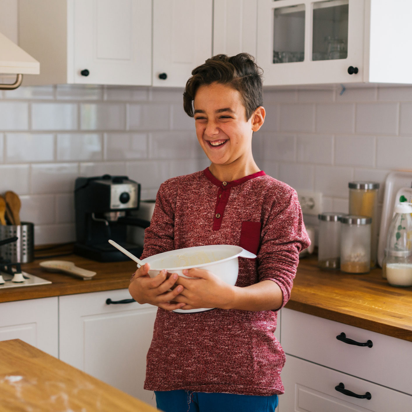 A young boy smiles as he holds a colorful bowl filled with snacks in his hands.