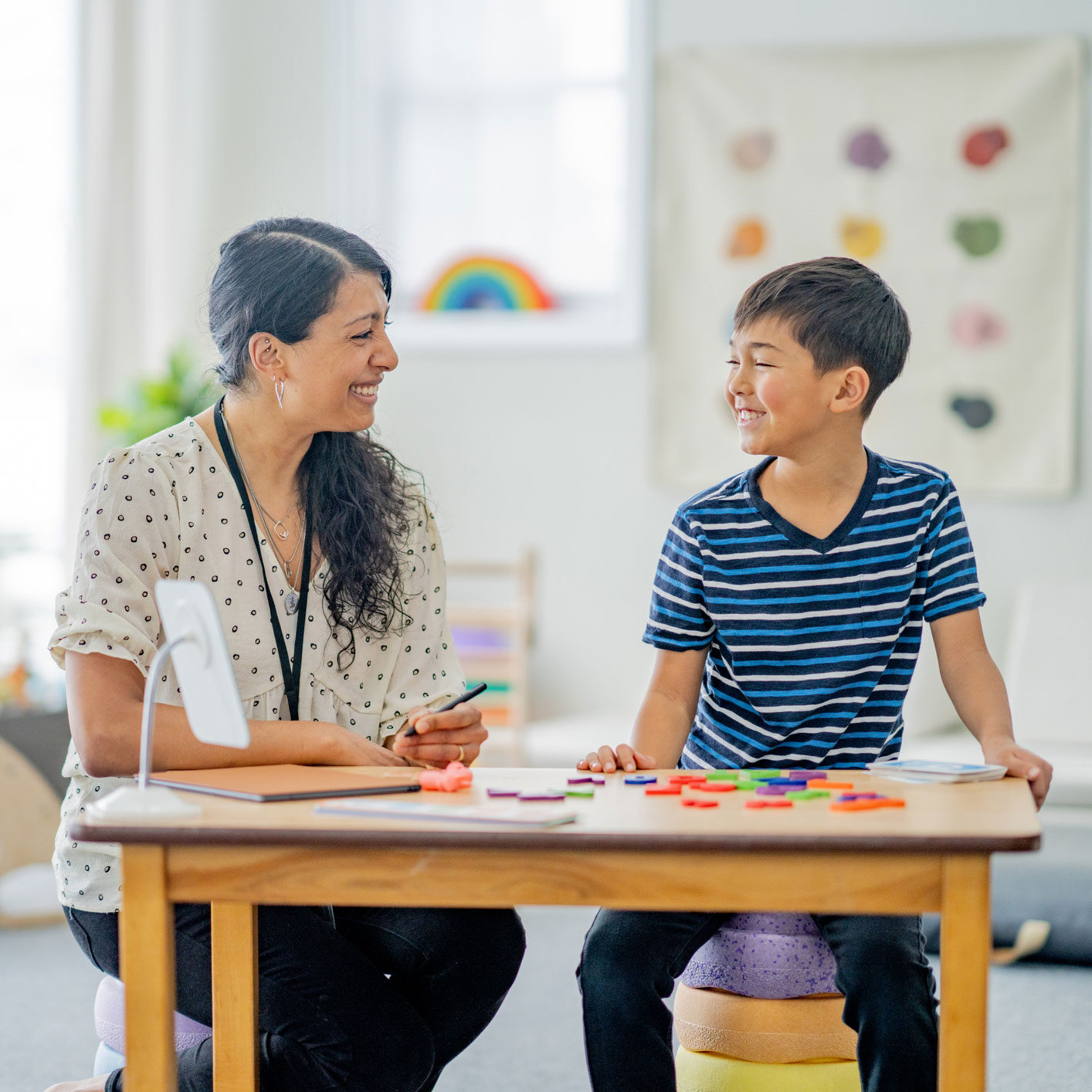 A woman and a boy are seated at a classroom table, engaged in a learning activity together.