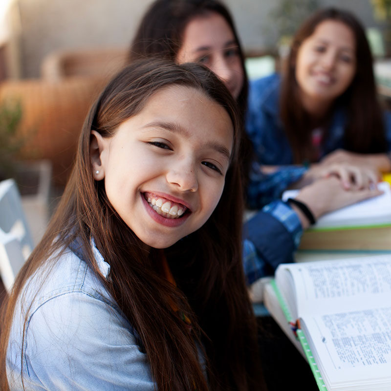 A group of girls gathered around a table, engaged in reading and discussing their books together.